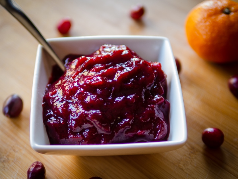 Cranberry sauce in a white bowl with cranberries scattered on the table beside it.