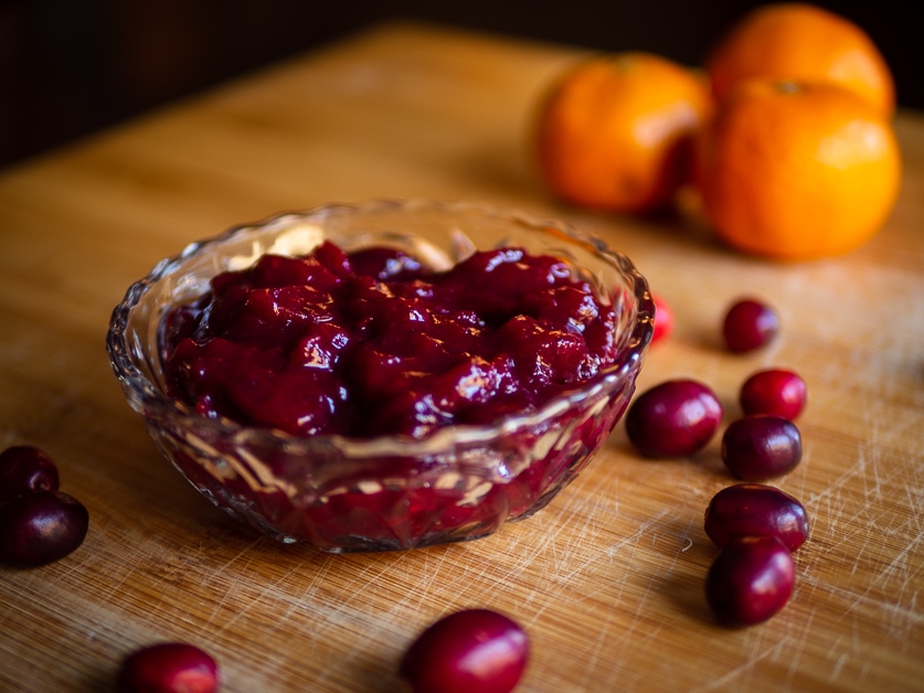 Frozen cranberry sauce in a bowl with a pile of oranges in the background and 