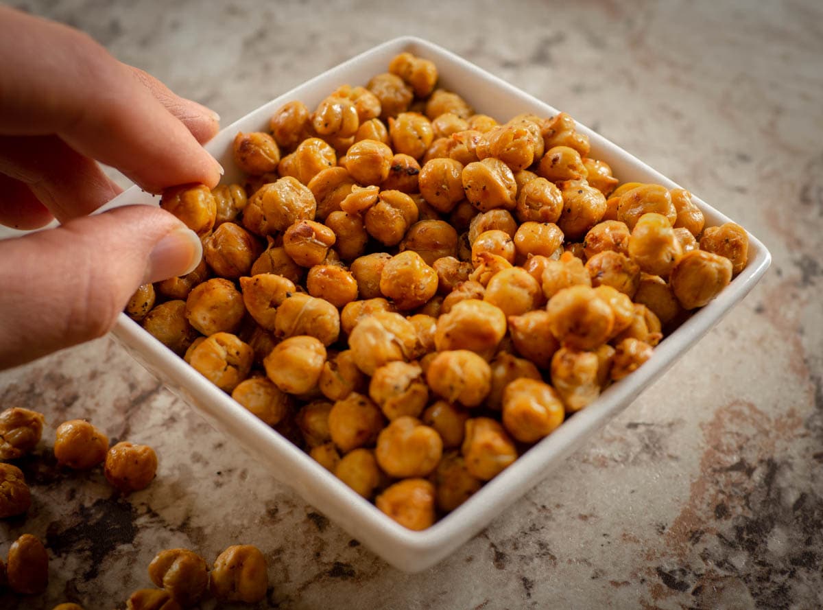Roasted Chickpeas in a bowl with a hand taking a bite.