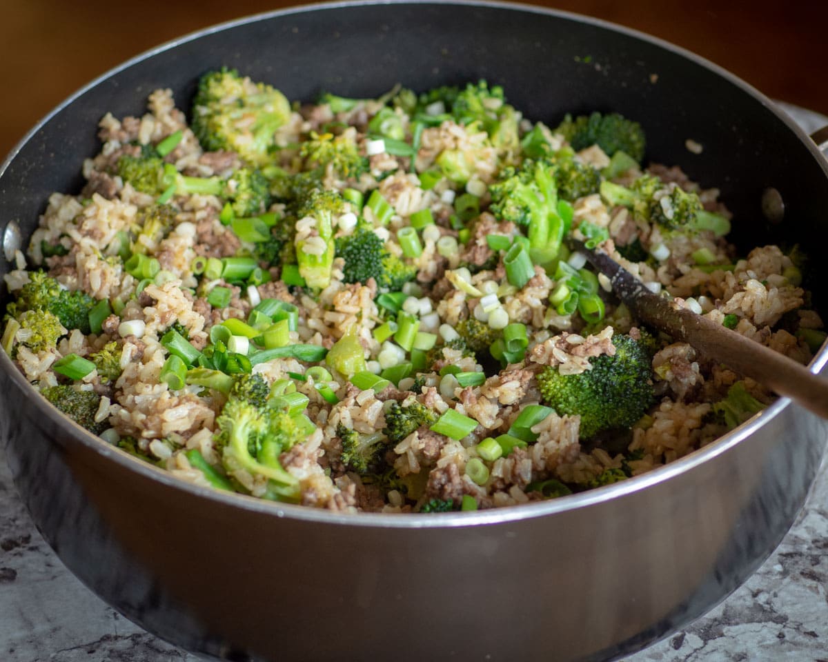 Ground beef and broccoli in a skillet with a wooden spoon.