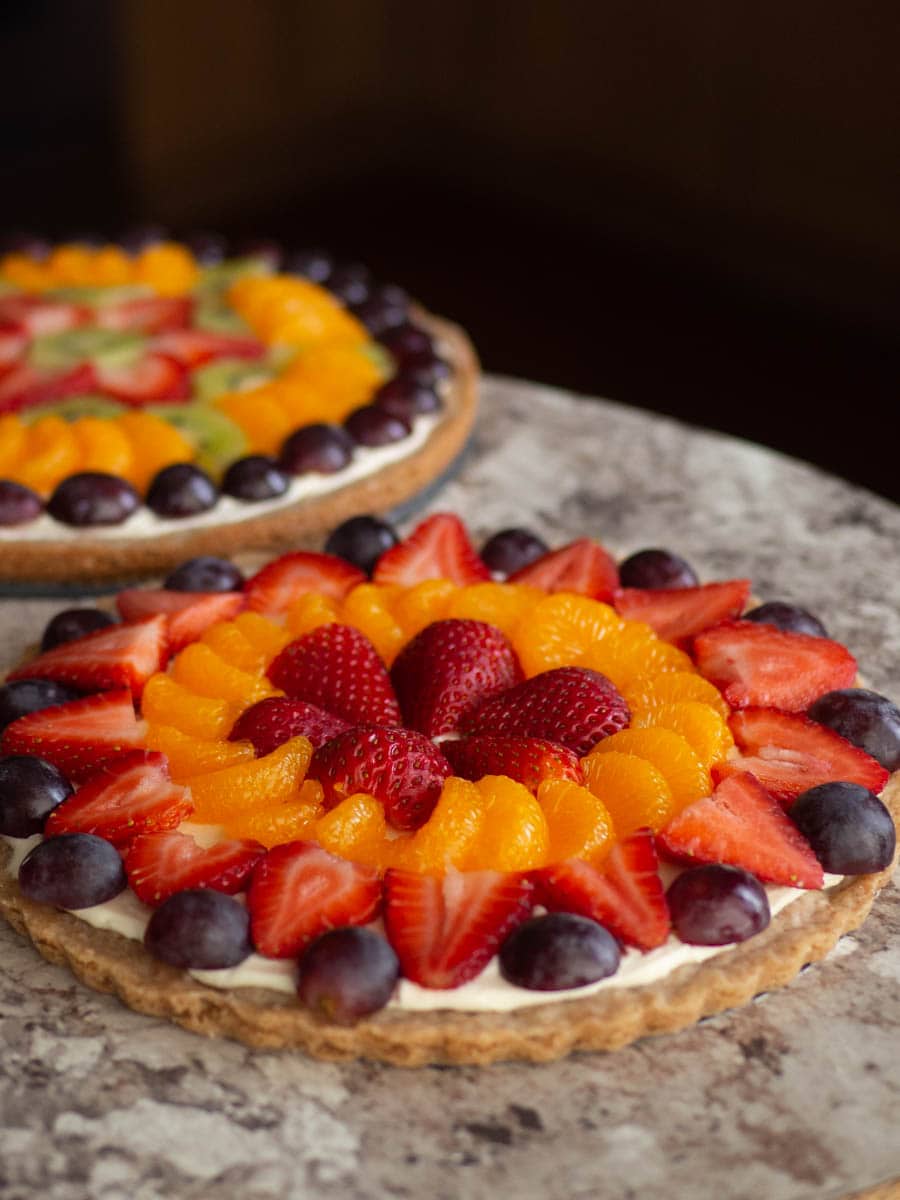 Two assembled fruit pizzas sitting on a countertop.