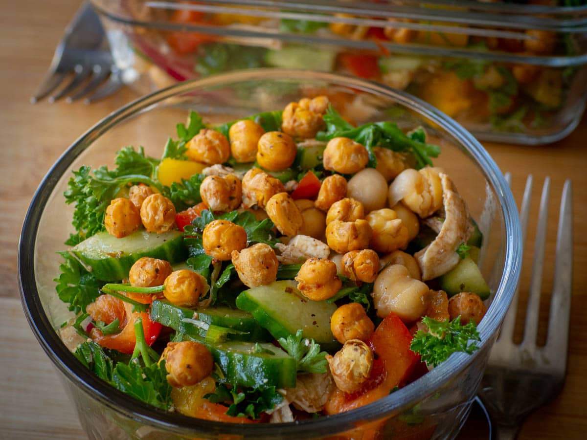 Mediterranean salad in a glass container topped with roasted chickpeas.