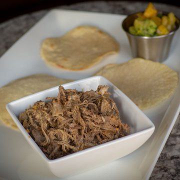 Pork Carnitas in a bowl with tortillas on a plate.