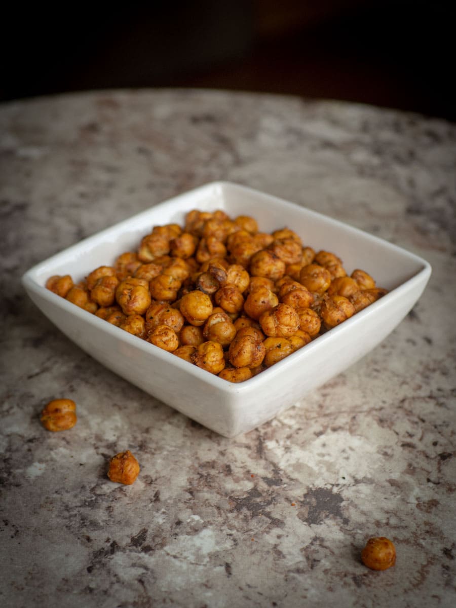 Bowl of roasted chickpeas with a few extras spilled on the countertop.