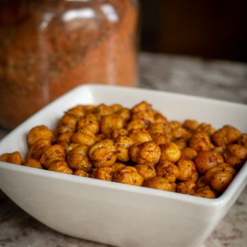 Bowl of chickpeas with a jar of Cajun seasoning in the background.