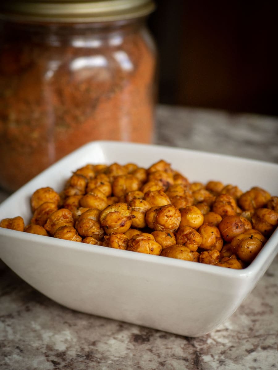 Bowl of chickpeas with a jar of Cajun seasoning in the background.