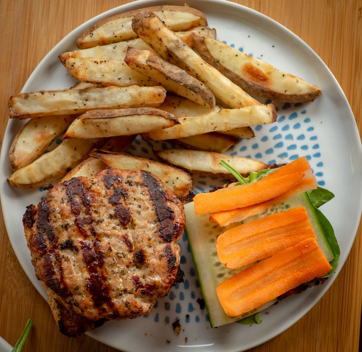 Burger on a plate topped with fresh carrots and cucumbers.