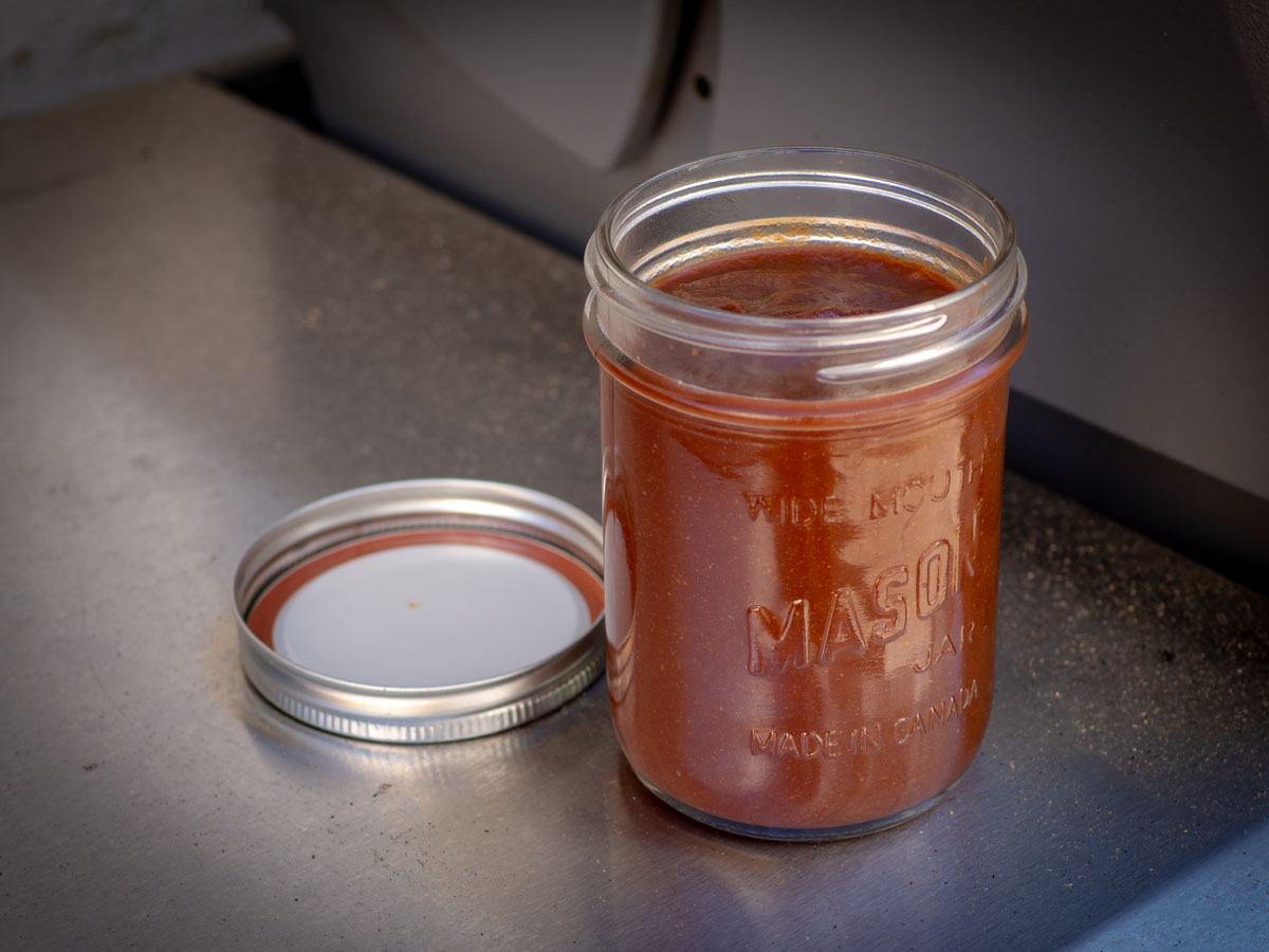 Jar of barbecue sauce sitting on the edge of a barbecue.