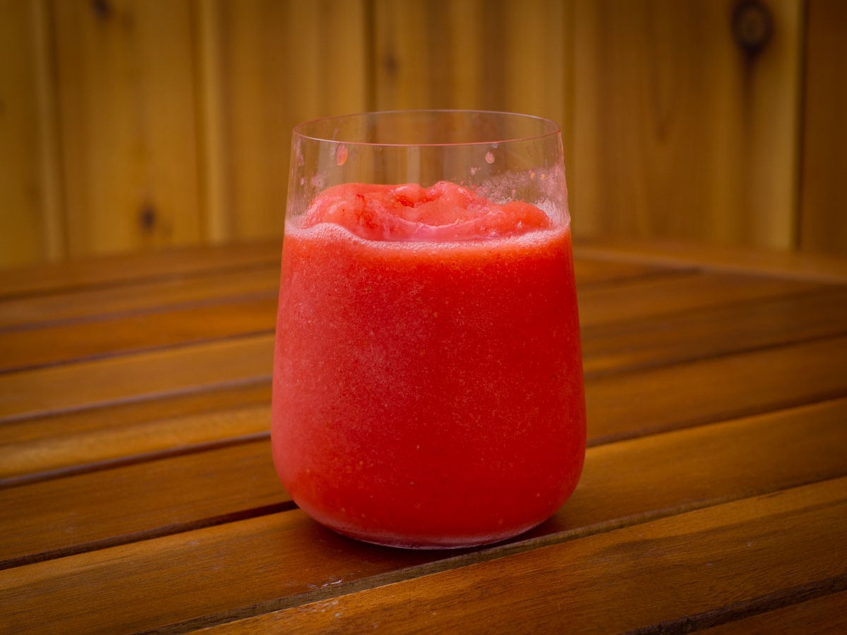 Frozen strawberry lemonade in a glass sitting on a wooden table outdoors.