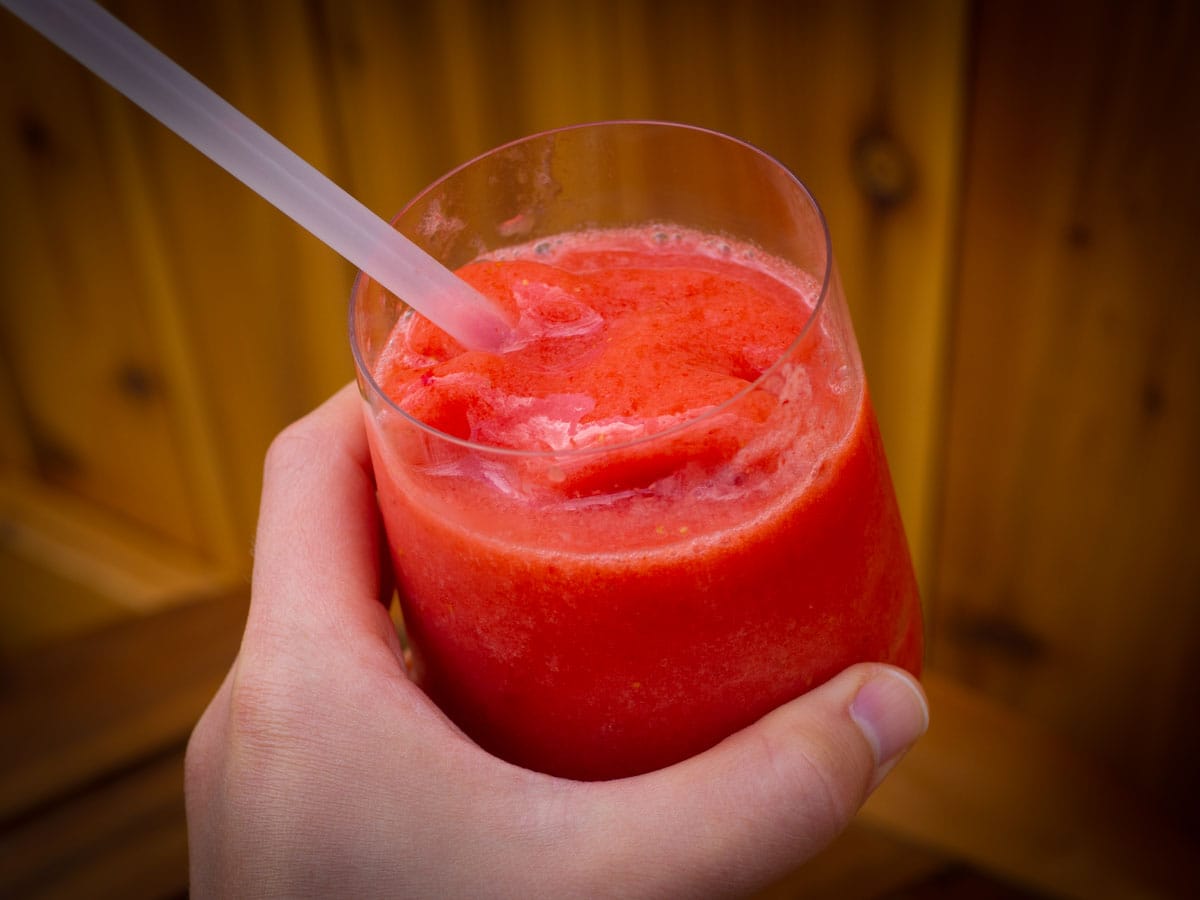 Hand holding a glass of frozen strawberry lemonade.