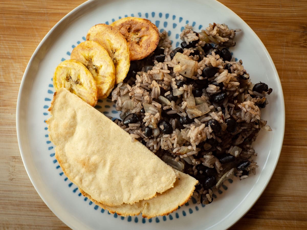 Black beans and rice on a plate with tortillas and plantains.