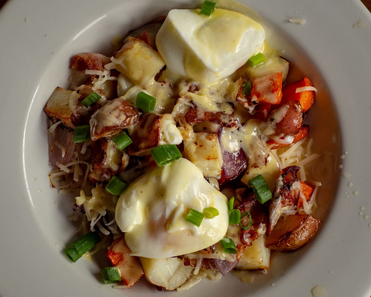 Bowl of breakfast potatoes topped with poached eggs and Hollandaise sauce.