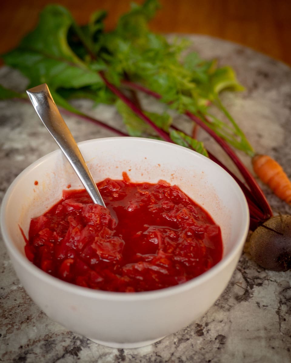 Bowl of pink soup with carrots and beets in the background.