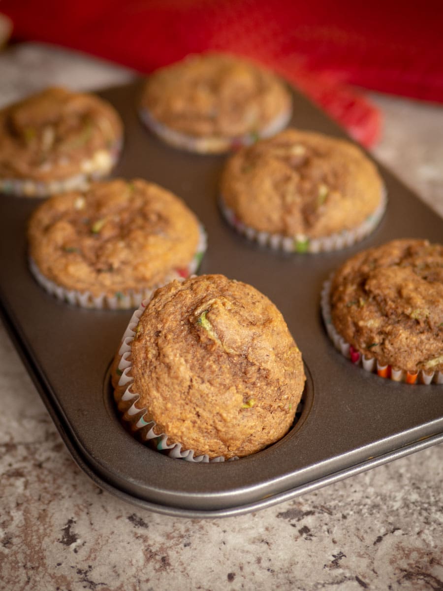 Zucchini spice muffins in a muffin tin with a red oven mitt in the background.