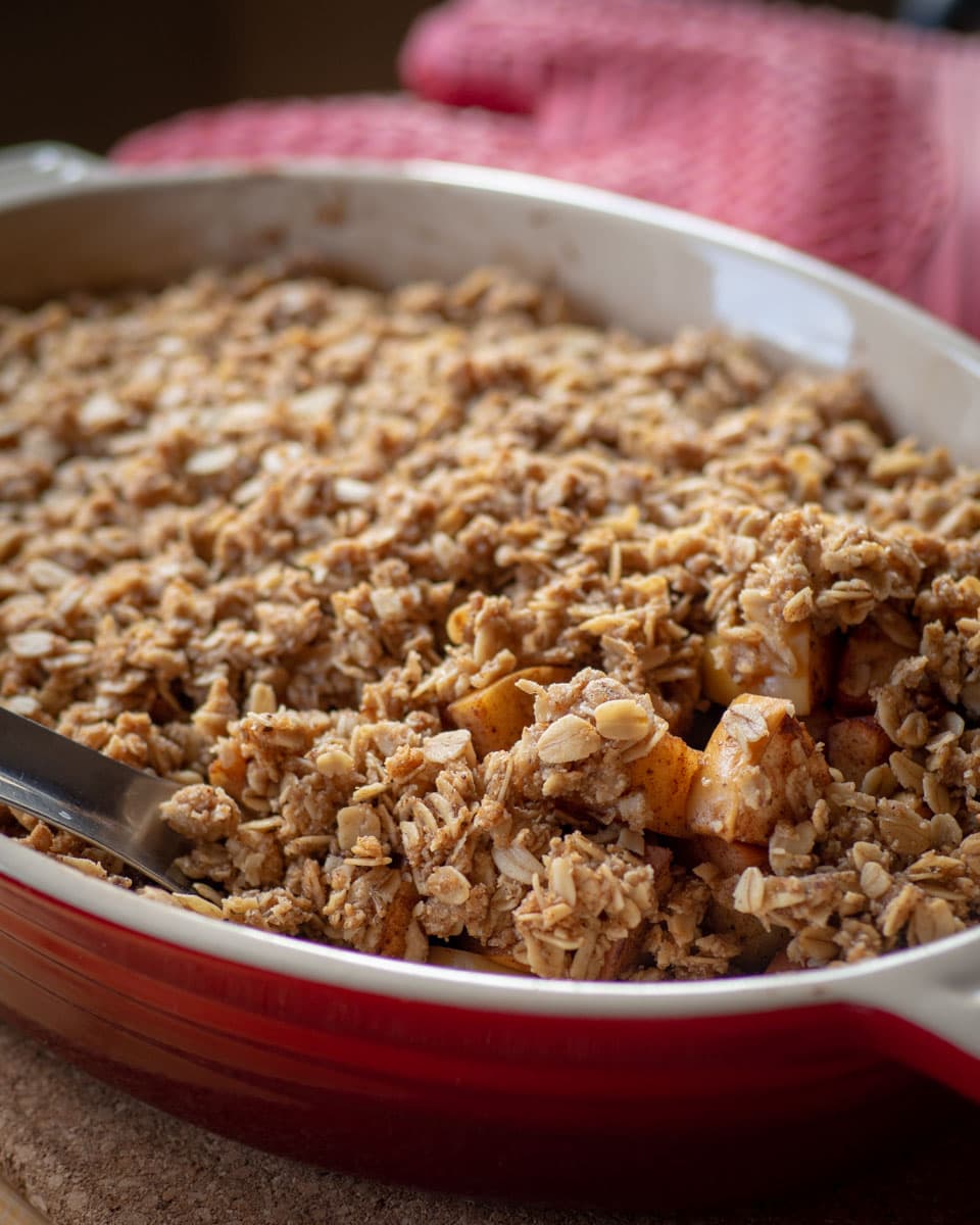 Spoon scooping a serving of apple crisp out of a baking dish.