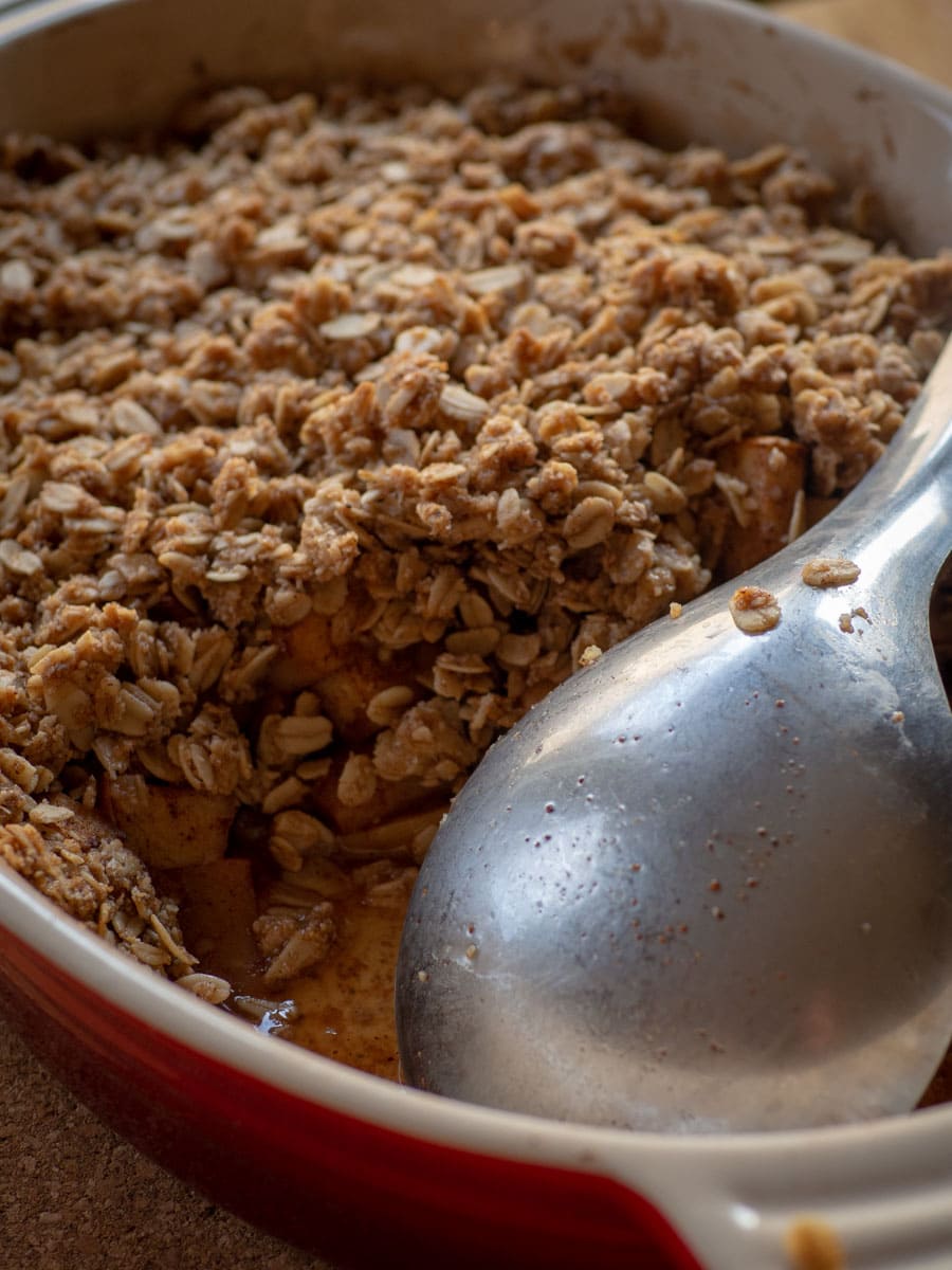 Oat flour apple crisp in a baking dish with a scoop taken out.