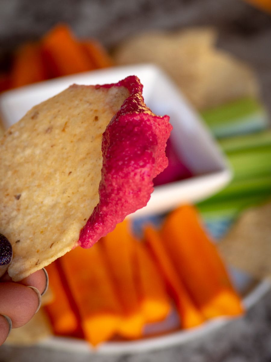 Tortilla chip dipped in pink beet hummus.