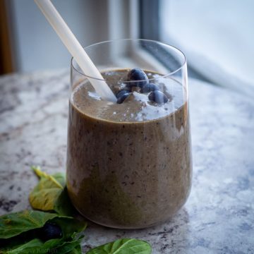 Blueberry smoothie in a glass with a straw.