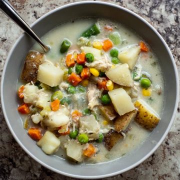 Bowl of creamy soup with potatoes, vegetables and chicken.