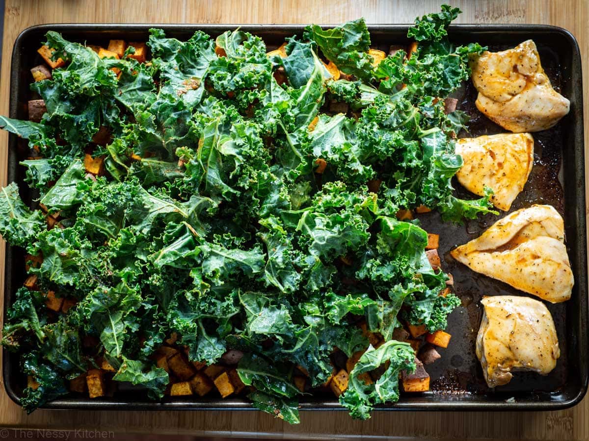 Kale placed on top of a sheet pan with sweet potatoes and chicken.