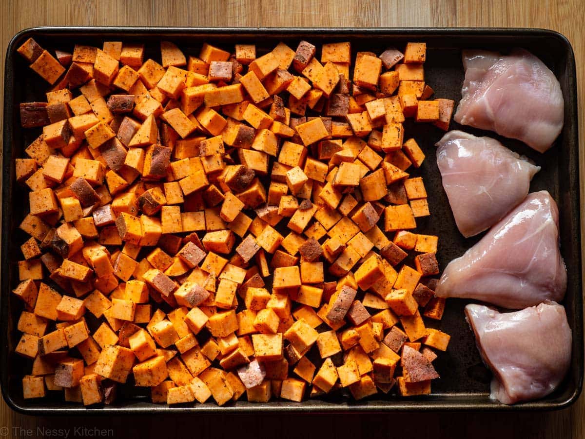 Sweet potatoes and raw chicken on a sheet pan.