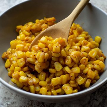 Bowl of corn with a wooden spoon.