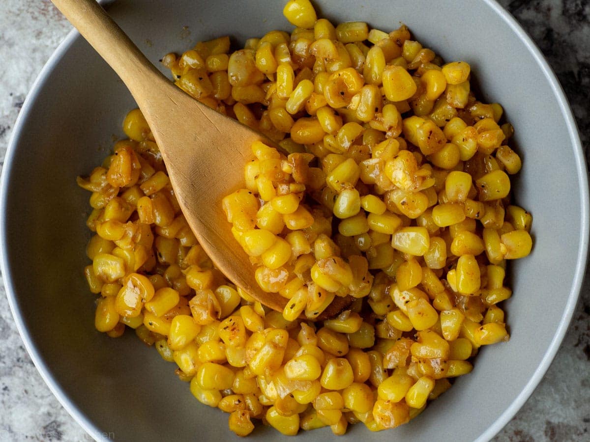 Cajun corn in a bowl with a wooden spoon.