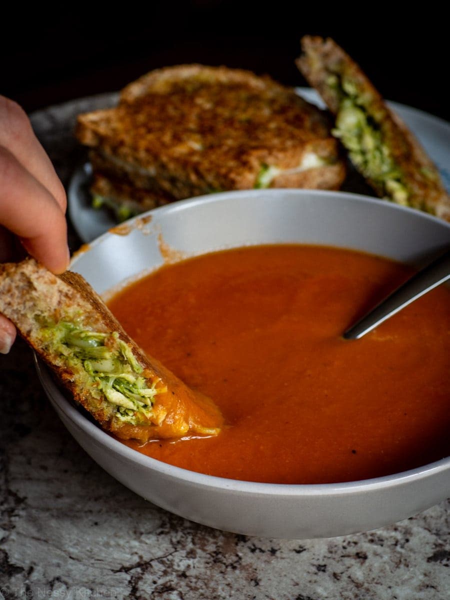 Hand dipping a chicken sandwich into a bowl of tomato soup.