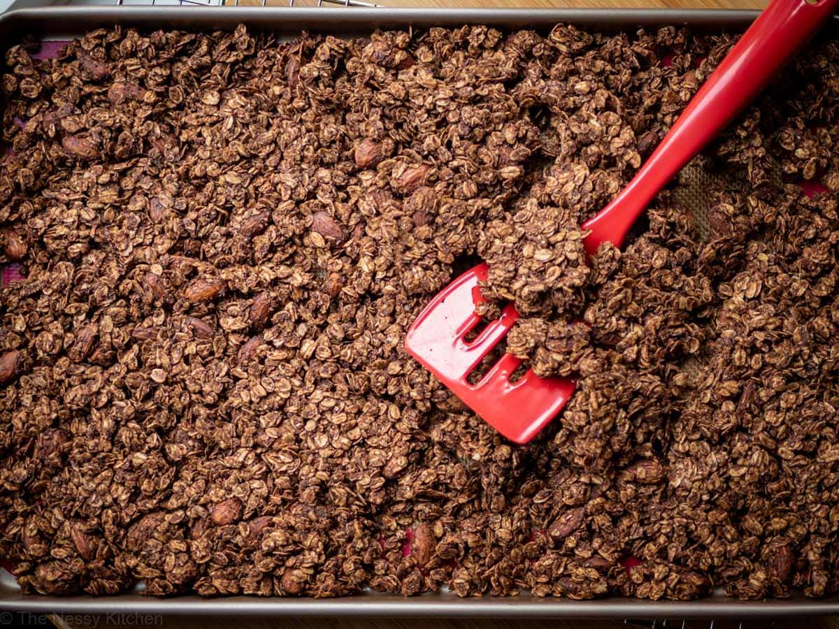 Chocolate granola on a sheet pan with a red flipper.