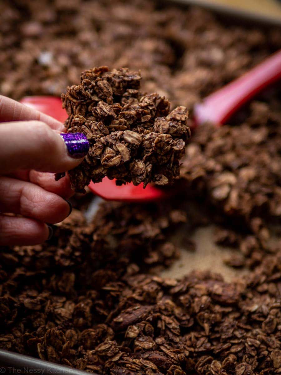 Hand holding a cluster of chocolate granola from a sheet pan.