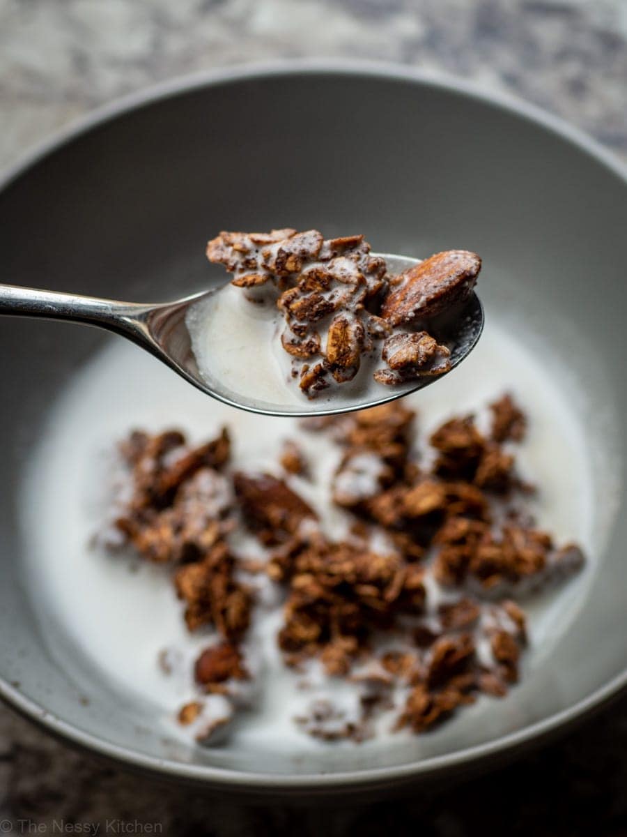 Chocolate granola in a bowl with milk and on a spoon.