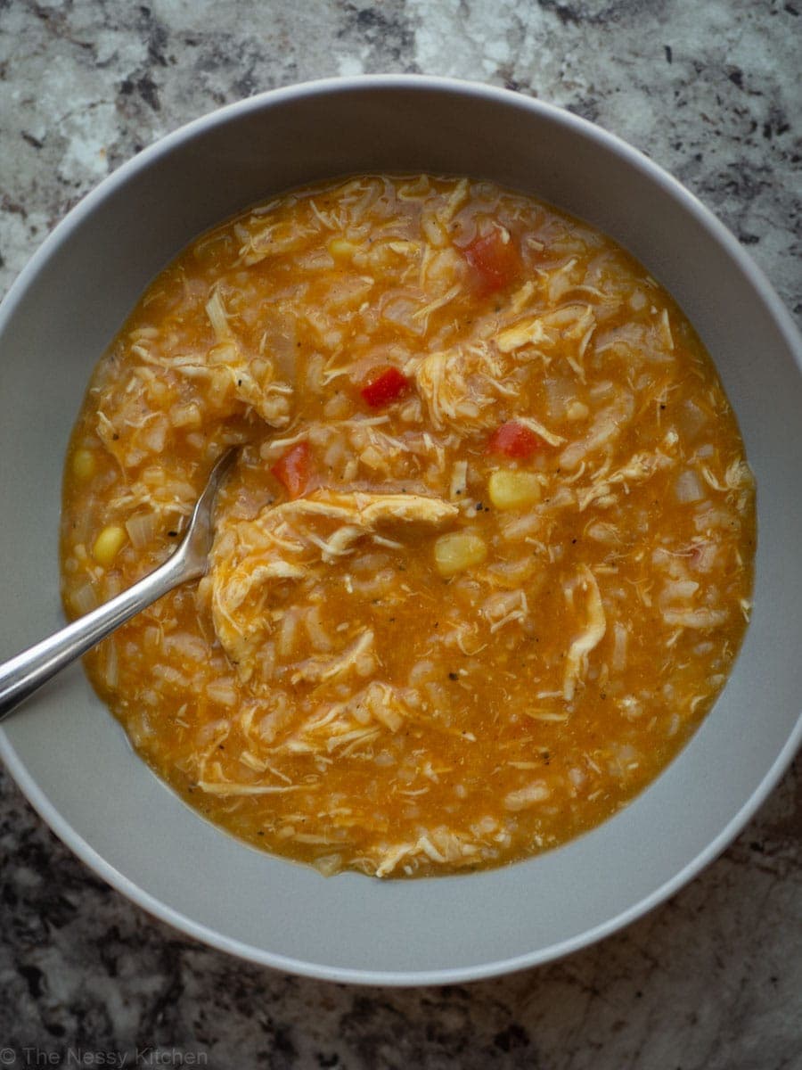 Top view of a bowl of pumpkin soup with visible pieces of peppers, corn and rice.