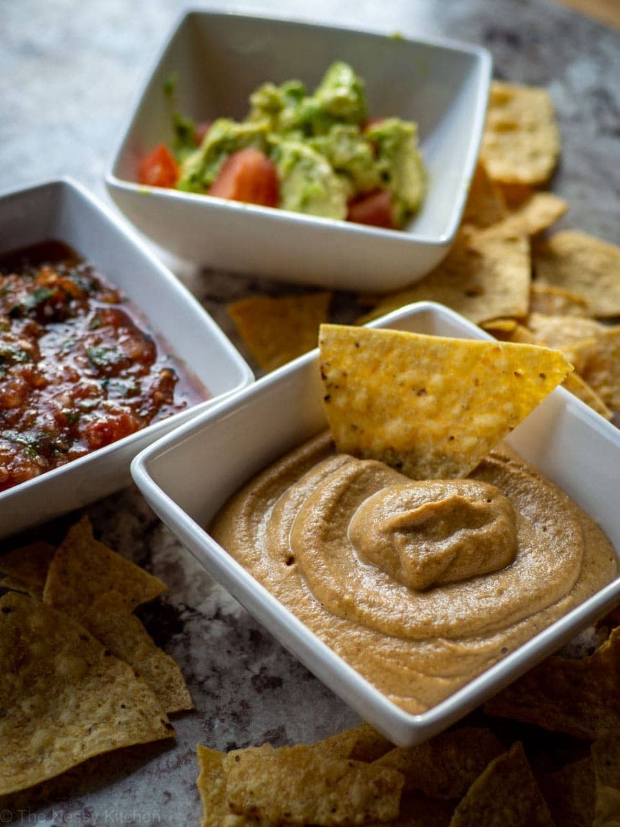 Queso with tortilla chips, guacamole and salsa in the background