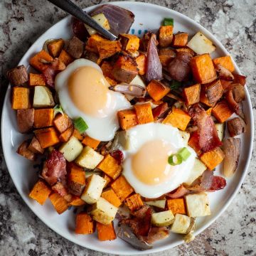 Plate of roasted potatoes, sweet potatoes, bacon and eggs.