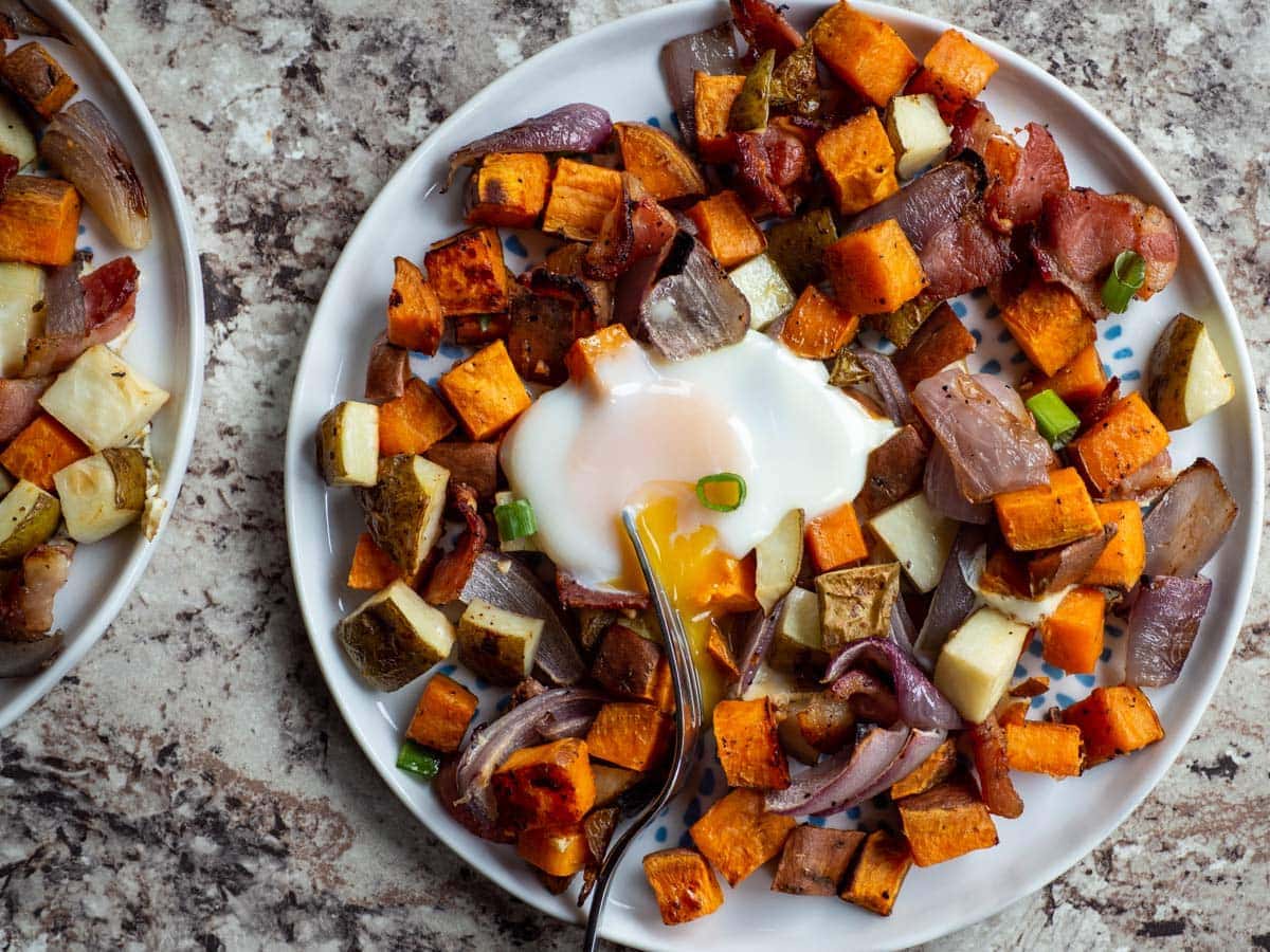 Top view of a plate of sweet potatoes, potatoes and onions with an egg on top.