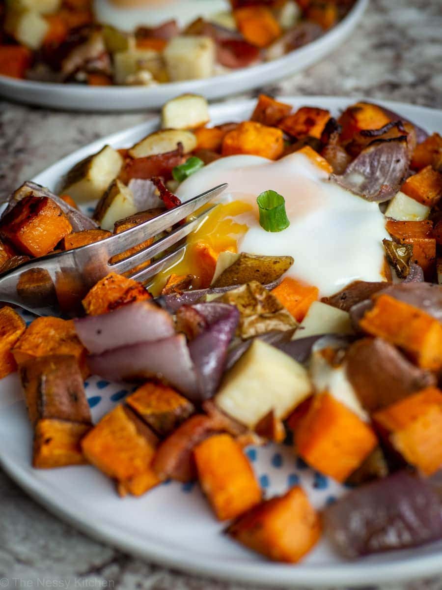 Close up shot of a runny egg yolk on a plate of roasted yams and potatoes.