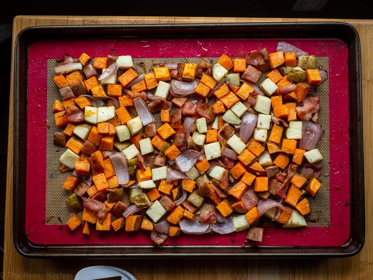 Cooked potatoes and bacon on a sheet pan pushed together to create a surface for cracking the eggs on.