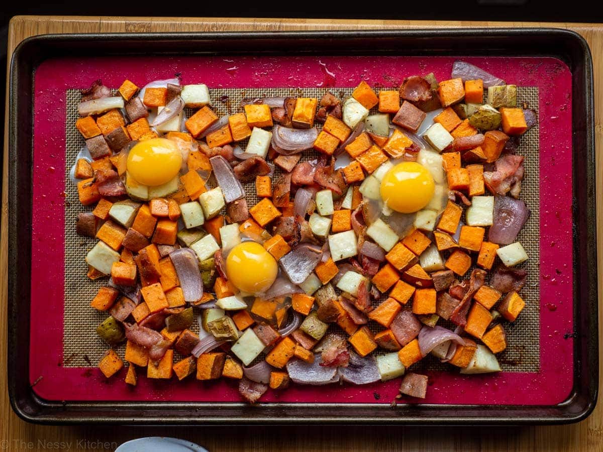 Eggs cracked on top of a sheet pan of roasted vegetables.