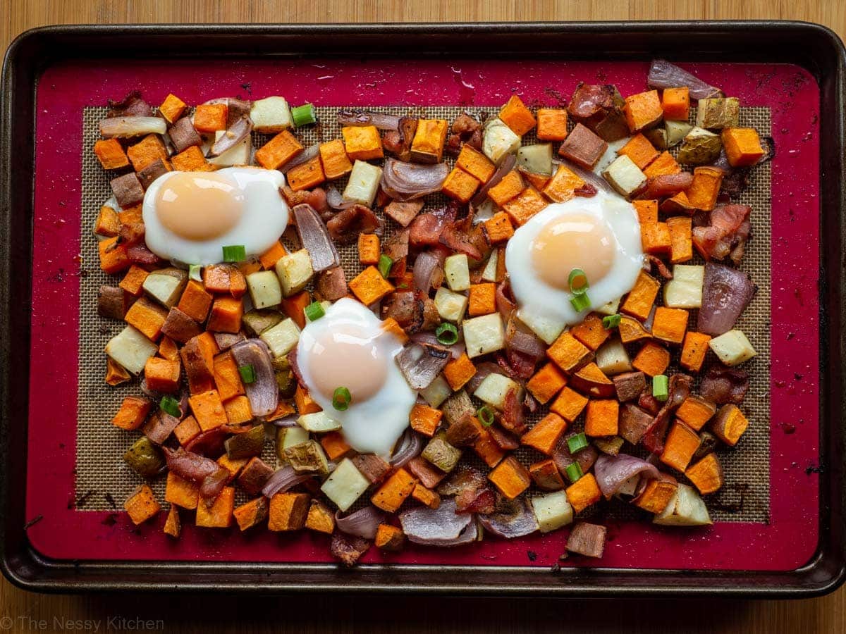 Cooked eggs on top of roasted vegetables on a sheet pan.