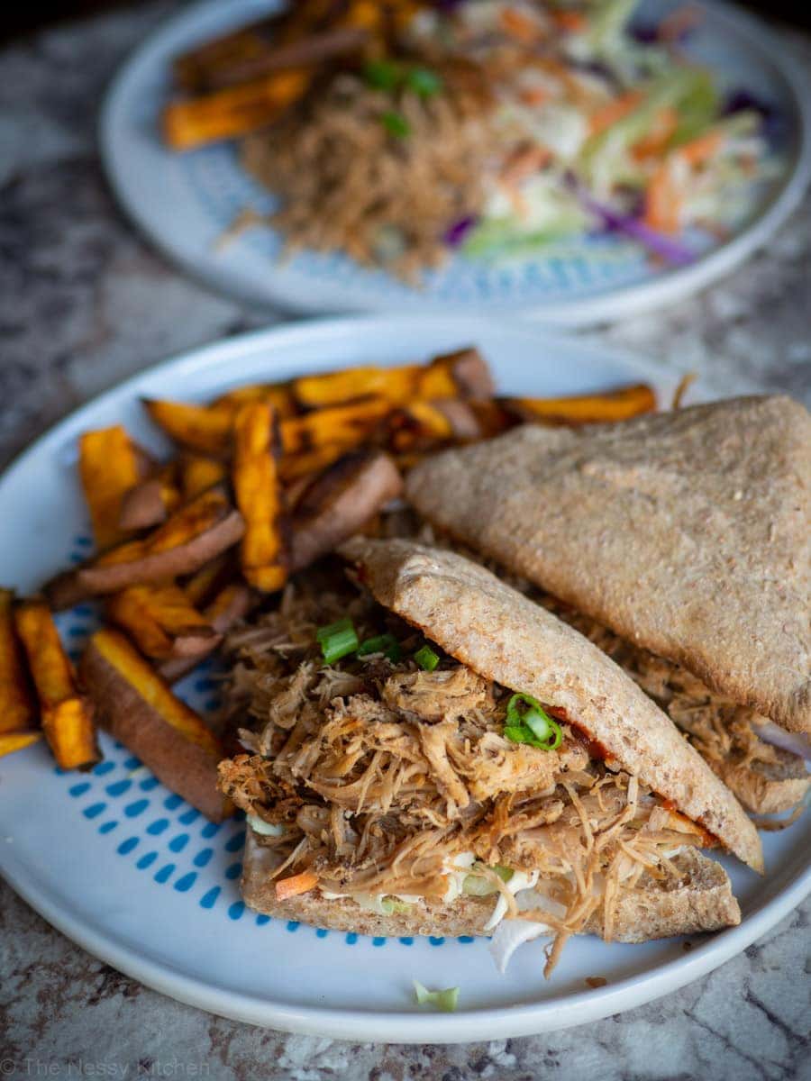 Pulled pork sandwich on a plate with coleslaw and sweet potato fries.