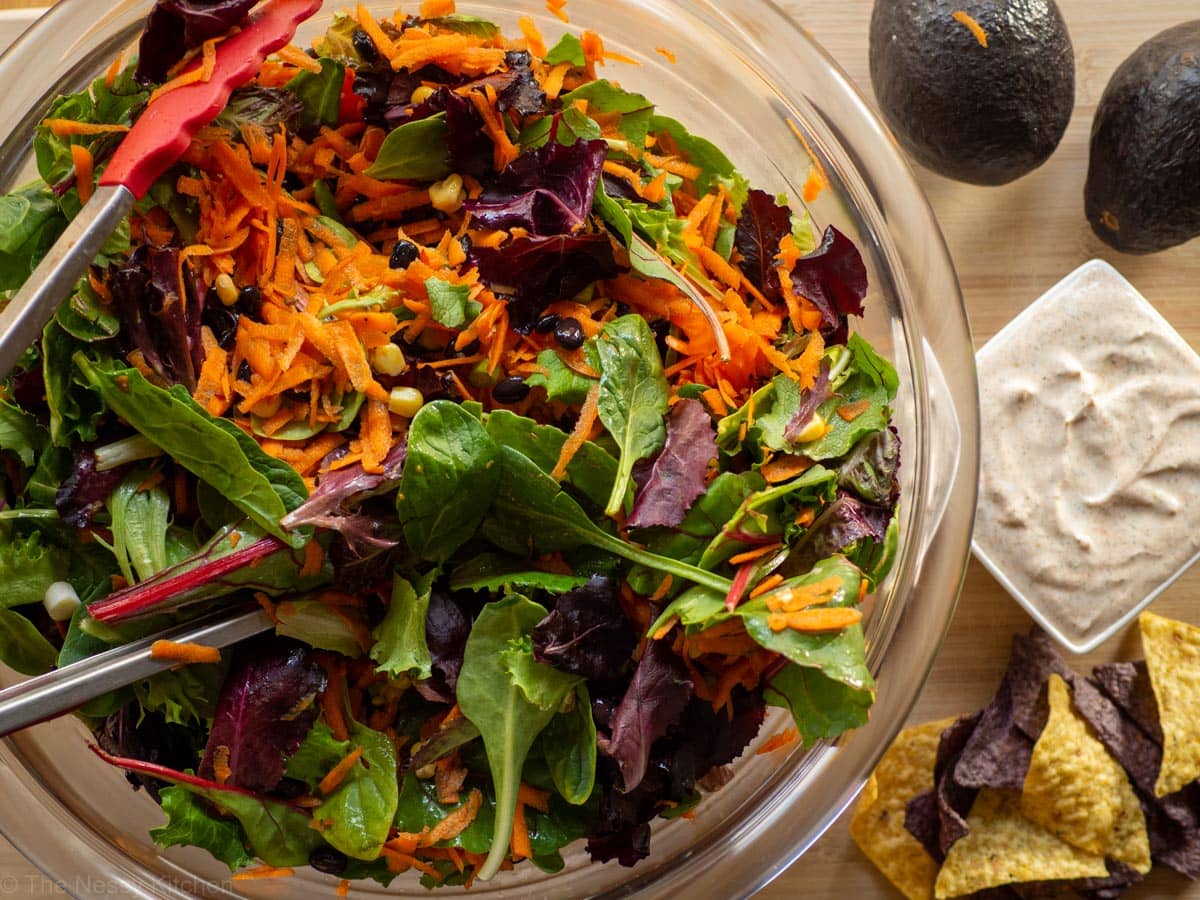 Salad mixed in a bowl with dressing on the side.