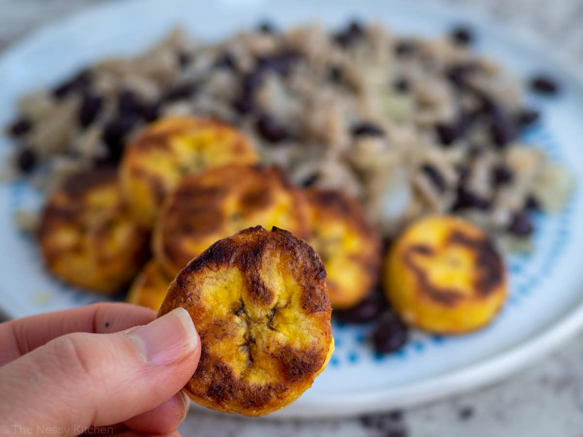 A baked ripe plantain round with gallo pinto in the background.