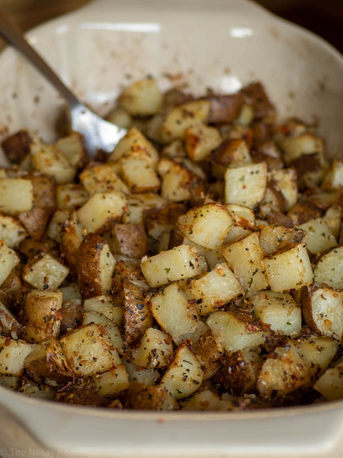 Baking pan of onion roasted potatoes with a serving spoon.