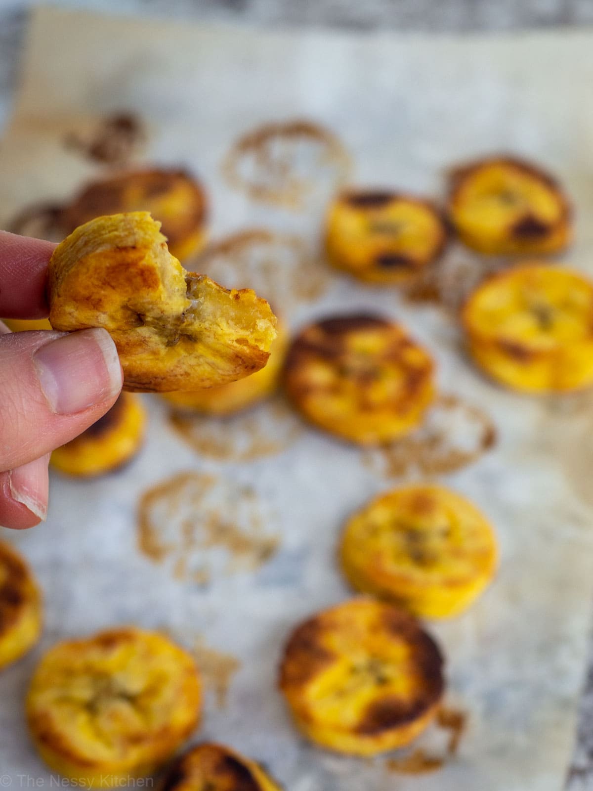 Hand holding a piece of plantain with a bite taken out.