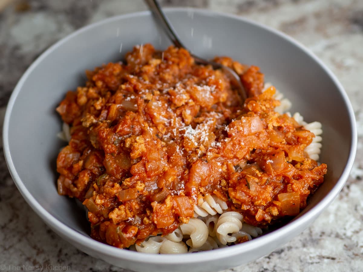 Parmesan grated onto a bowl of pasta with turkey spaghetti sauce.