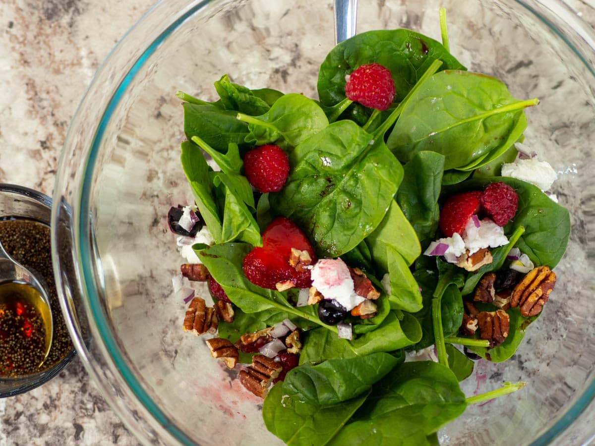 Mixing bowl filled with spinach, berries and cheese.