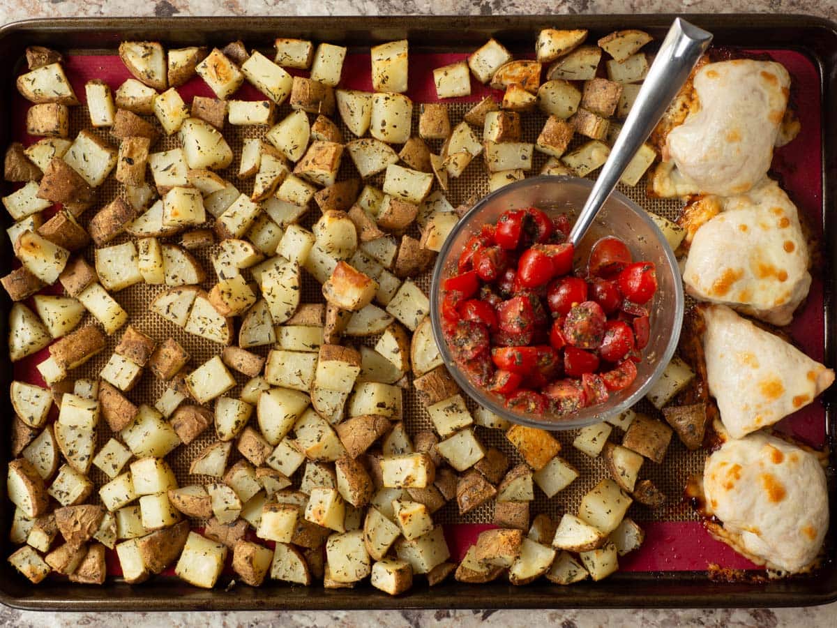 Sheet pan with cooked potatoes and chicken with a bowl of bruschetta in the centre.