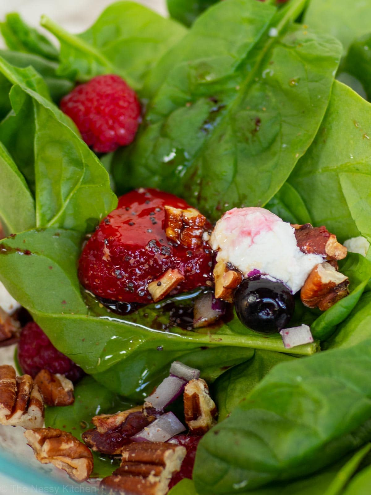 Close up shot of maple balsamic poppyseed dressing drizzled on a spinach salad.