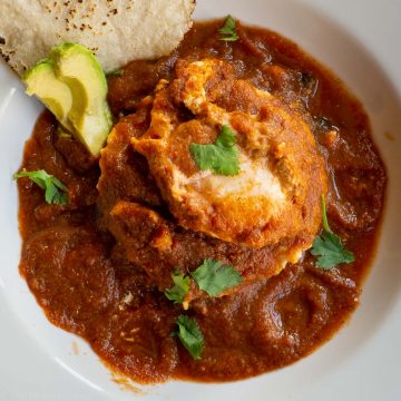 Top view of huevos rancheros with avocado and tortillas on the side.