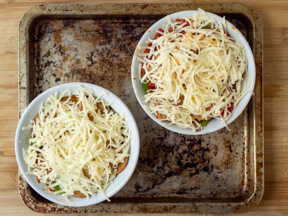 Unbaked pizza bowls in ramekins on top of a cookie sheet.